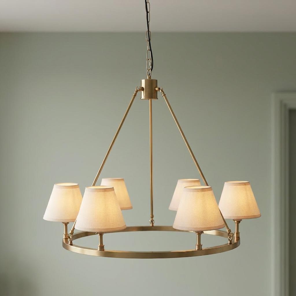 Brass circular pendant light with five small white fabric shades against a light green wall.