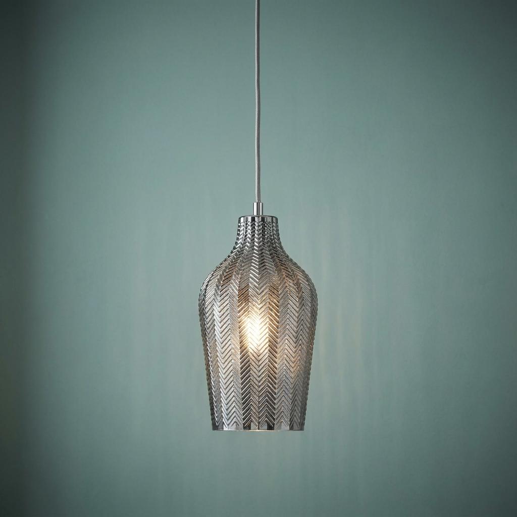 Smoked ribbed glass pendant light with a chevron pattern illuminated against a teal wall.