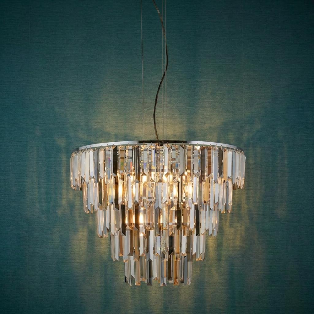 Tiered chrome pendant light with crystal prism drops glowing against a textured teal wall.