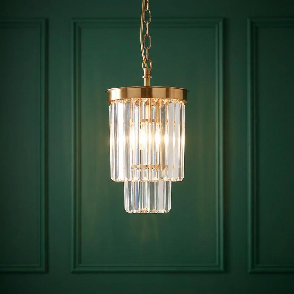 A brass pendant light with tiered clear cut glass crystals against a dark green paneled wall.
