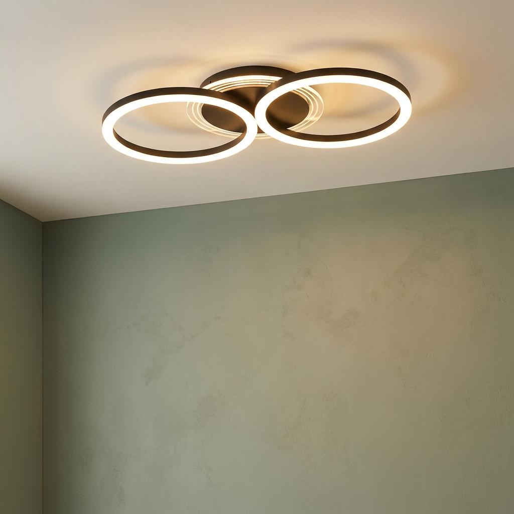 Modern black flush ceiling light with three interlocking illuminated rings on a white ceiling above a green wall.