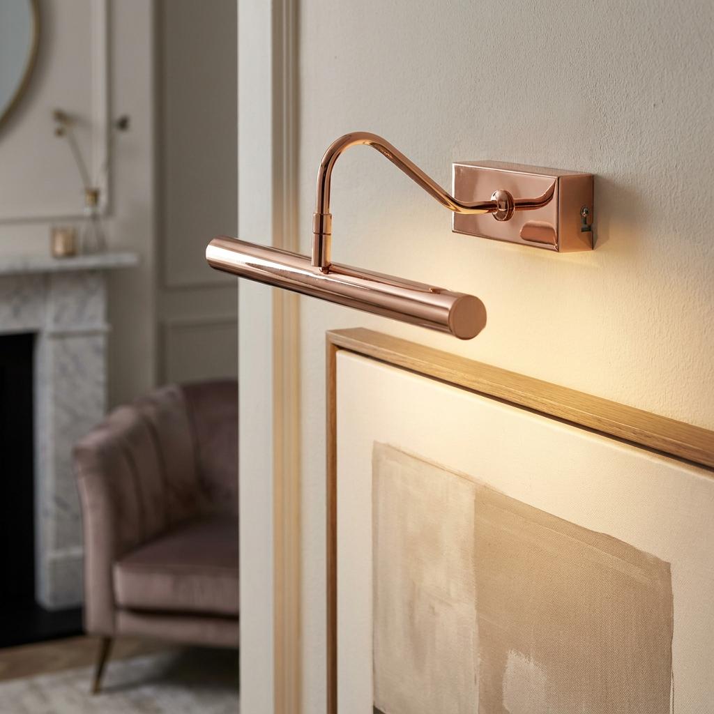 A copper LED picture light illuminating framed artwork on a wall in a contemporary living room setting.