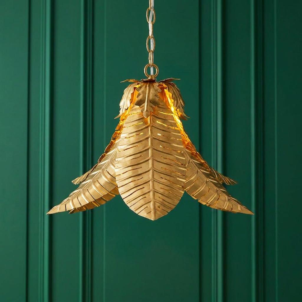 Distressed gold palm leaf ceiling pendant light glowing against a dark green paneled wall.