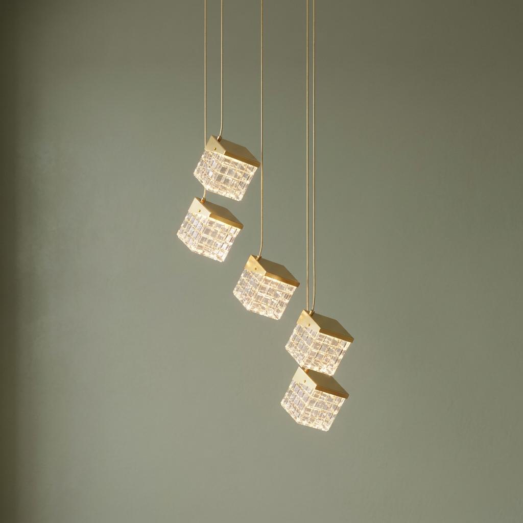 Five tiered cube pendant lights with satin brass finishes and textured glass shades against a green background.