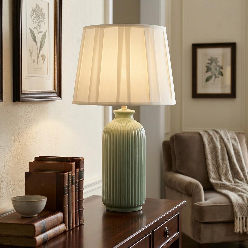 Dalian 1 light pale green ceramic table lamp with a pleated empire shade on a dark wooden sideboard.