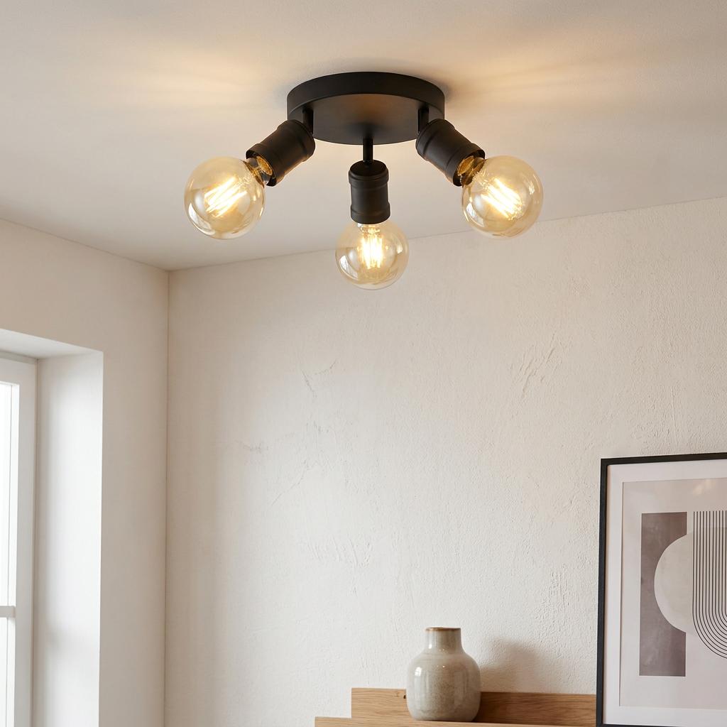 Modern three-light black flush ceiling fixture with warm-toned glass globe bulbs on a white textured ceiling.