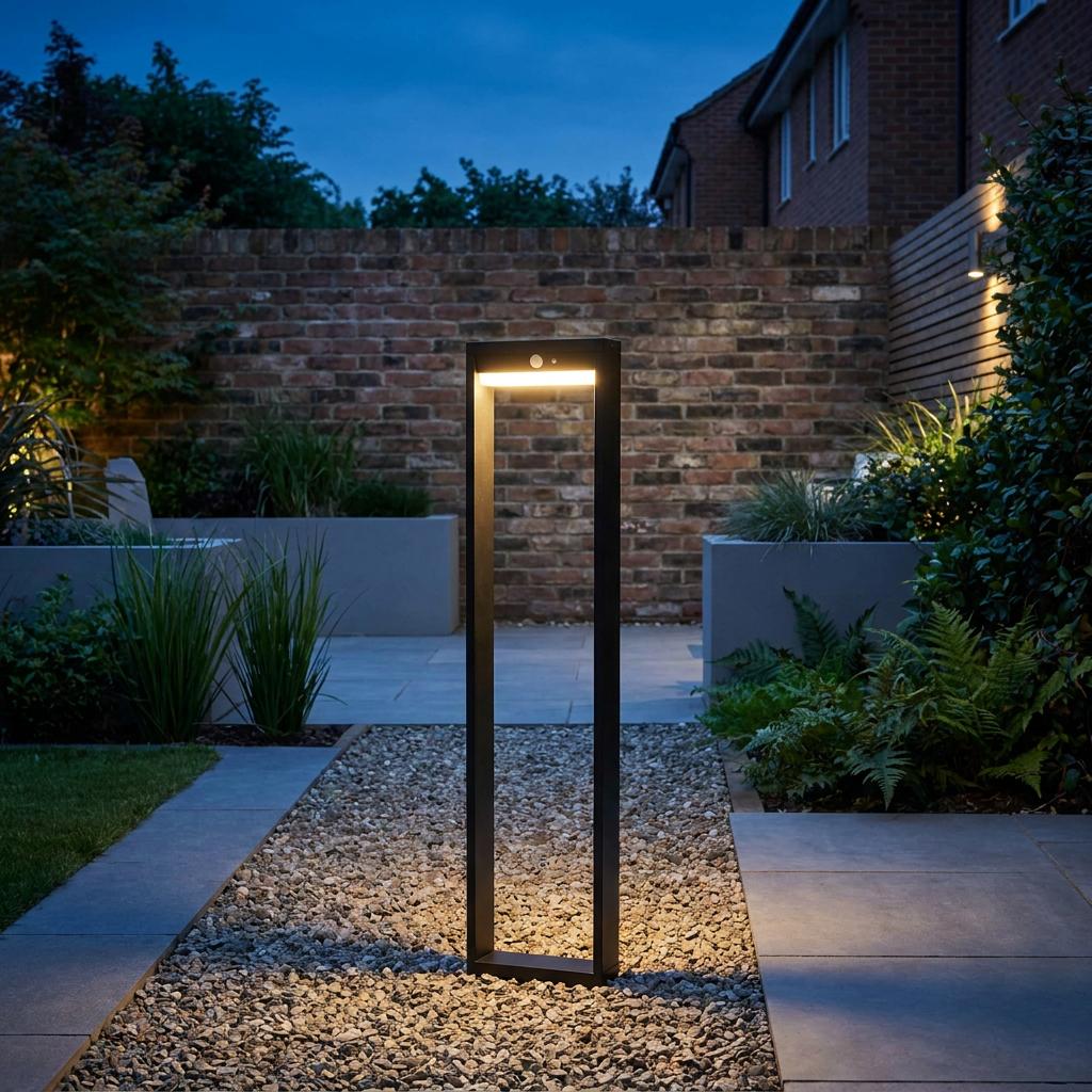 Modern black rectangular bollard light with PIR sensor illuminating a gravel path in a landscaped garden at night.