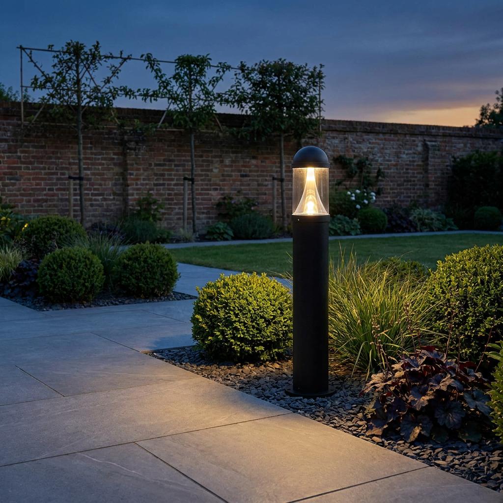 A black bollard light illuminating a tiled garden pathway and green shrubs at twilight.