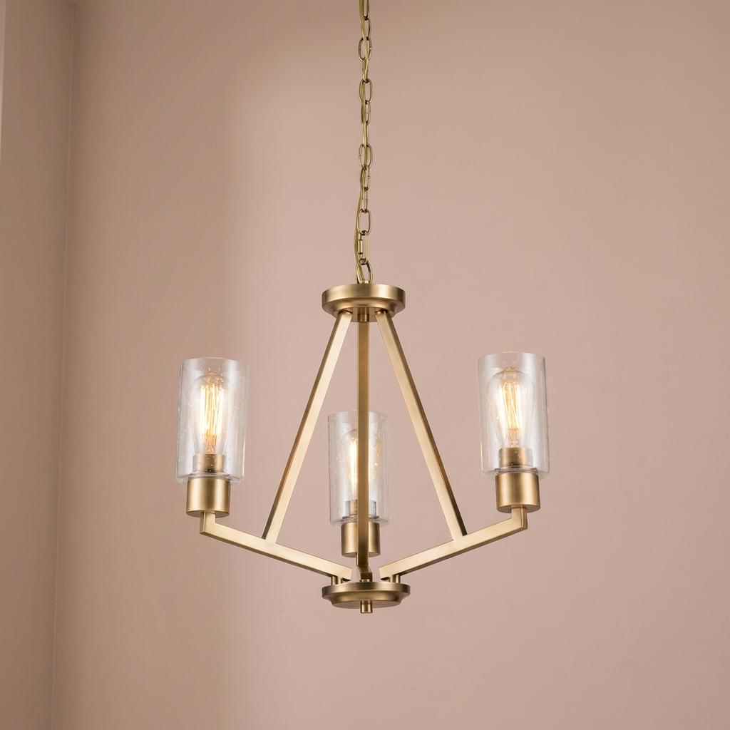 Three-light brass chandelier with clear seeded glass shades and vintage bulbs against a neutral wall.