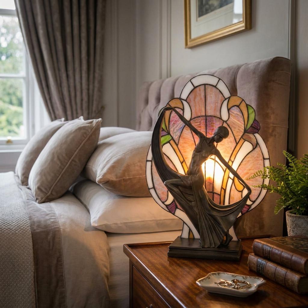 Art Deco Diane Tiffany bedside table lamp with a bronze dancer figurine on a wooden nightstand in a bedroom.
