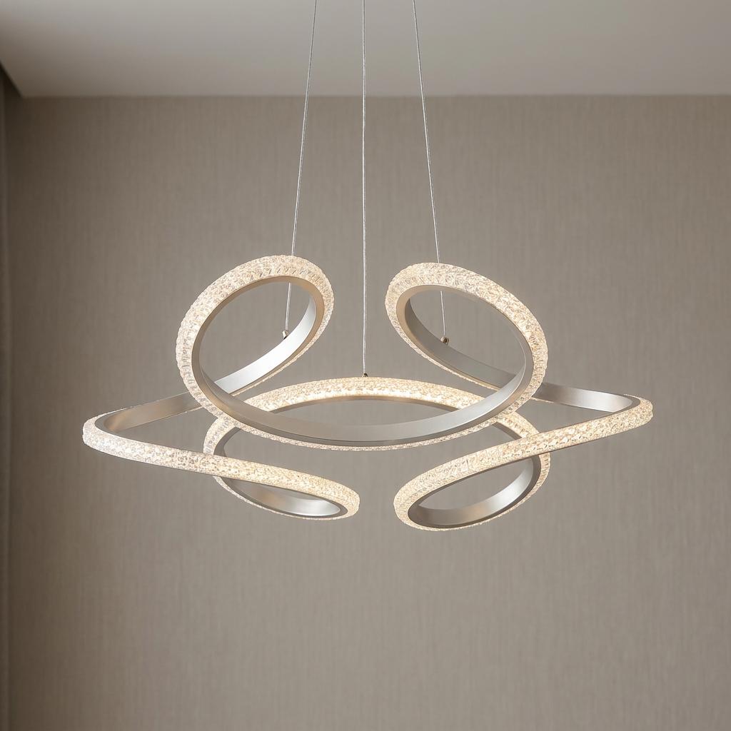 Abstract swirling LED pendant light in champagne metal with glowing crystal accents against a beige wall.