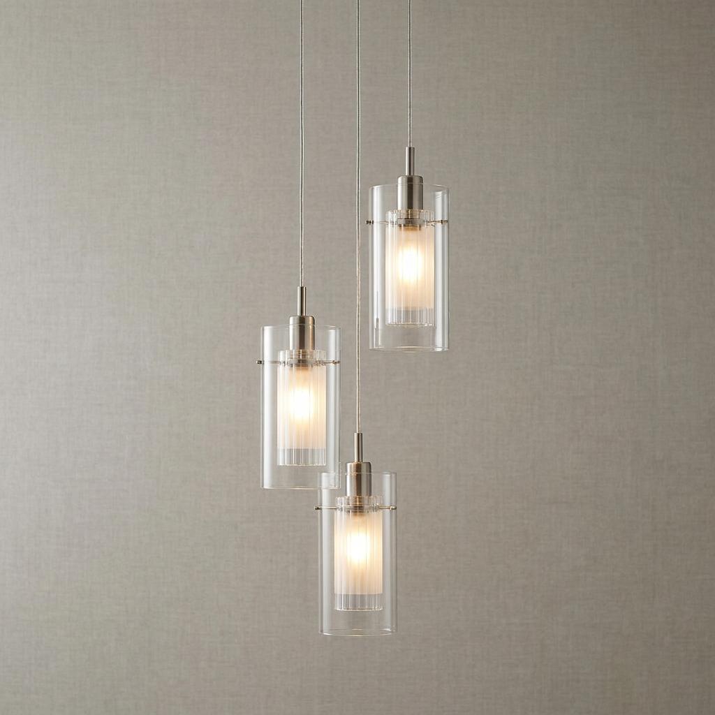 Staggered trio of chrome pendant lights with clear and frosted double glass shades against a textured wall.