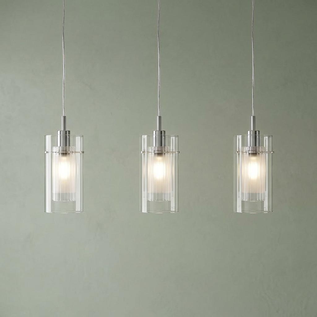 Three chrome pendant lights with nested glass cylinders glowing against a muted green wall.