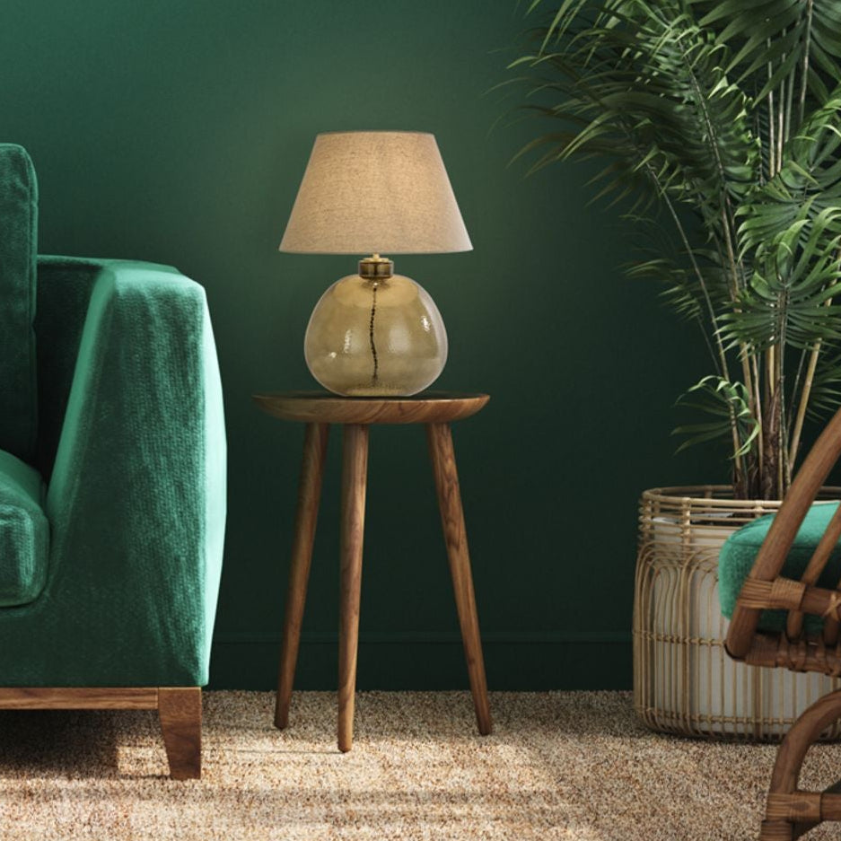Zenith green glass lamp glowing on a side table in a green velvet sofa lounge with rattan chair