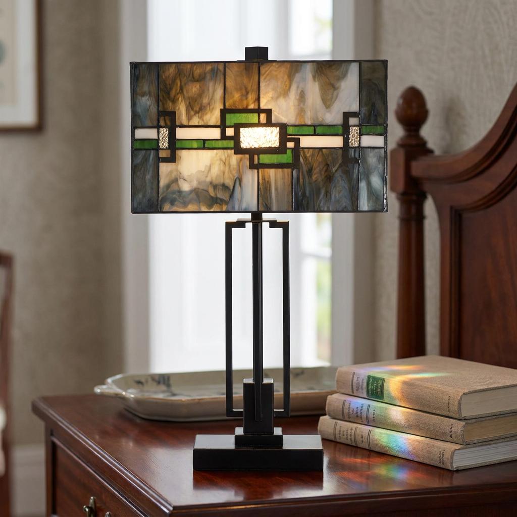 Rectangular Tiffany table lamp with a geometric green stained glass shade sitting on a wooden bedside table.