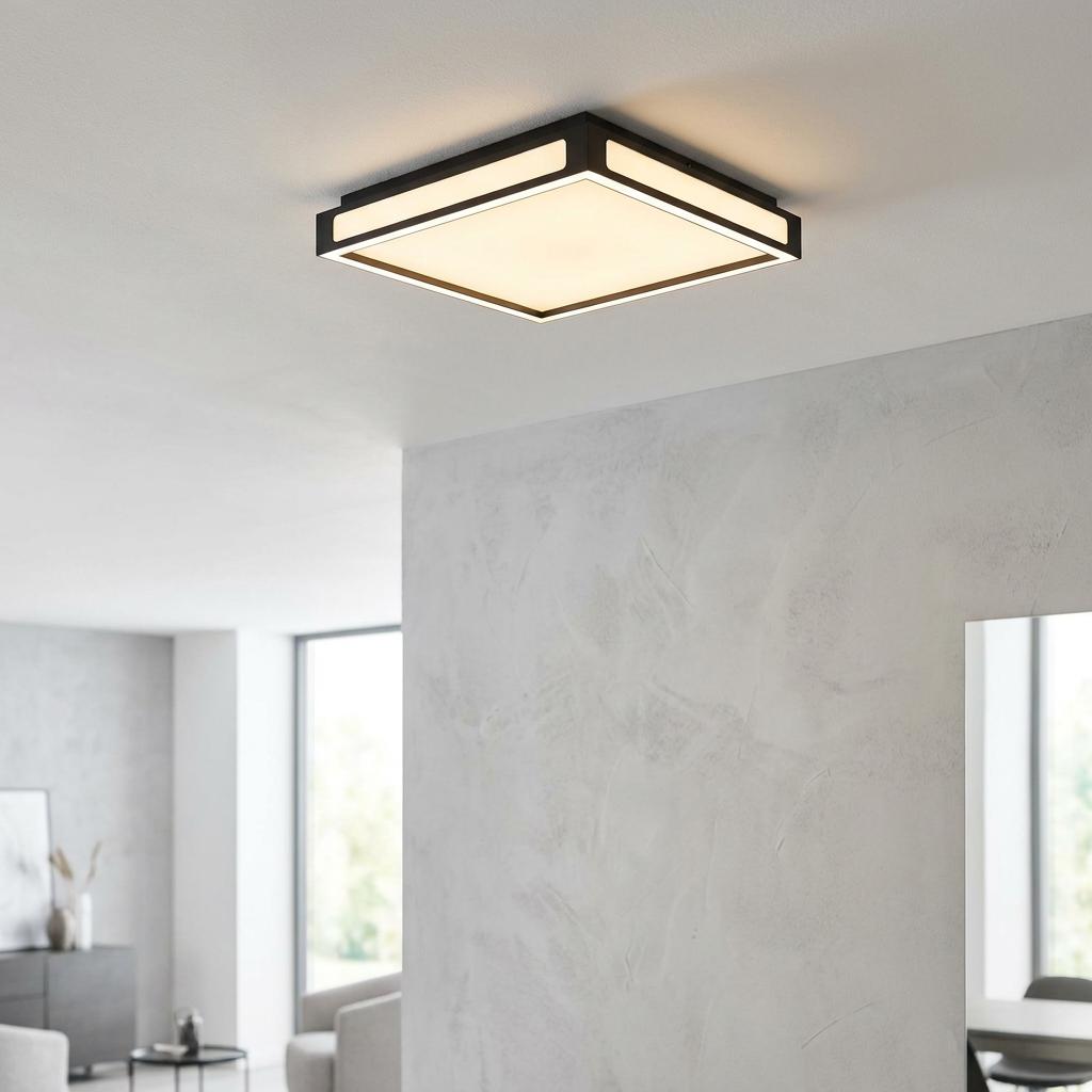 Square black-framed LED flush ceiling light illuminating a modern room with a textured grey wall.