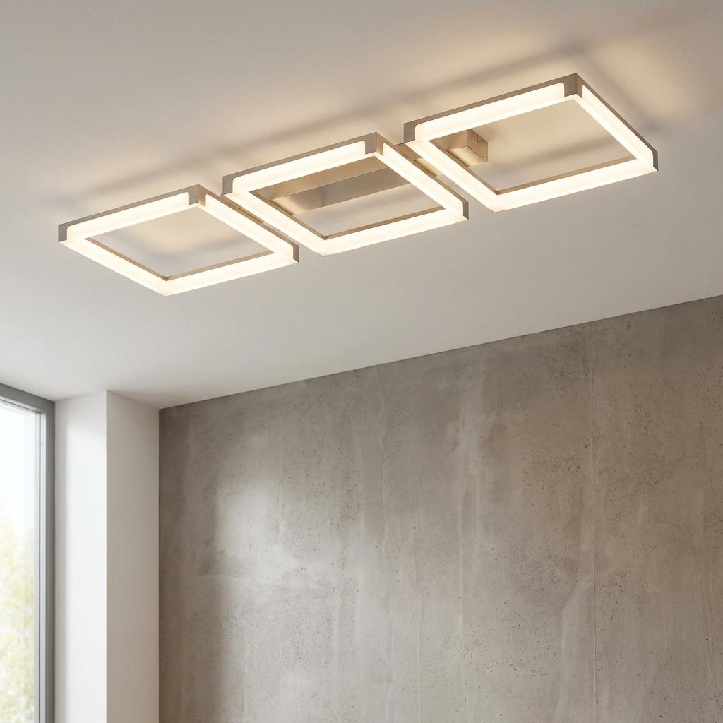Three square-shaped nickel-framed LED flush ceiling lights glowing warmly in a modern room with a concrete wall.