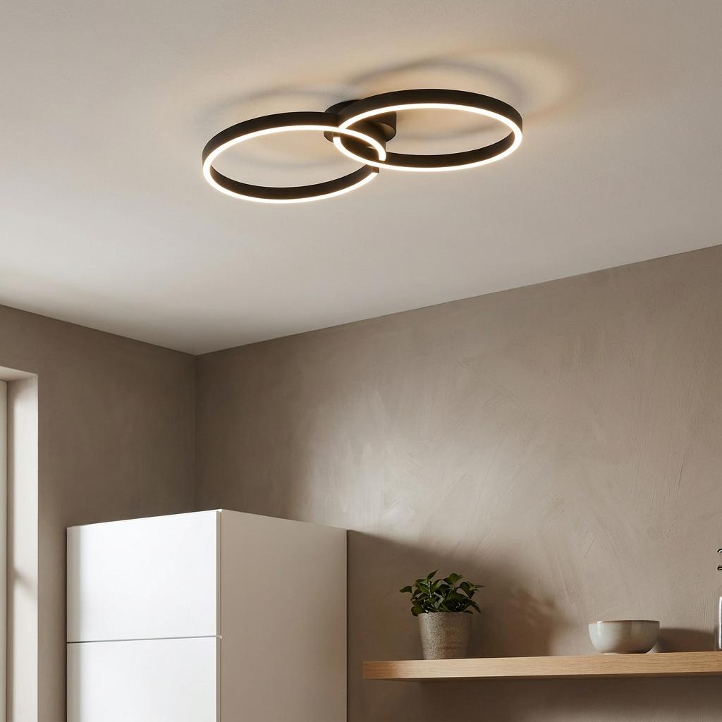 Modern black flush ceiling light with two interlocking LED rings mounted in a minimalist room.