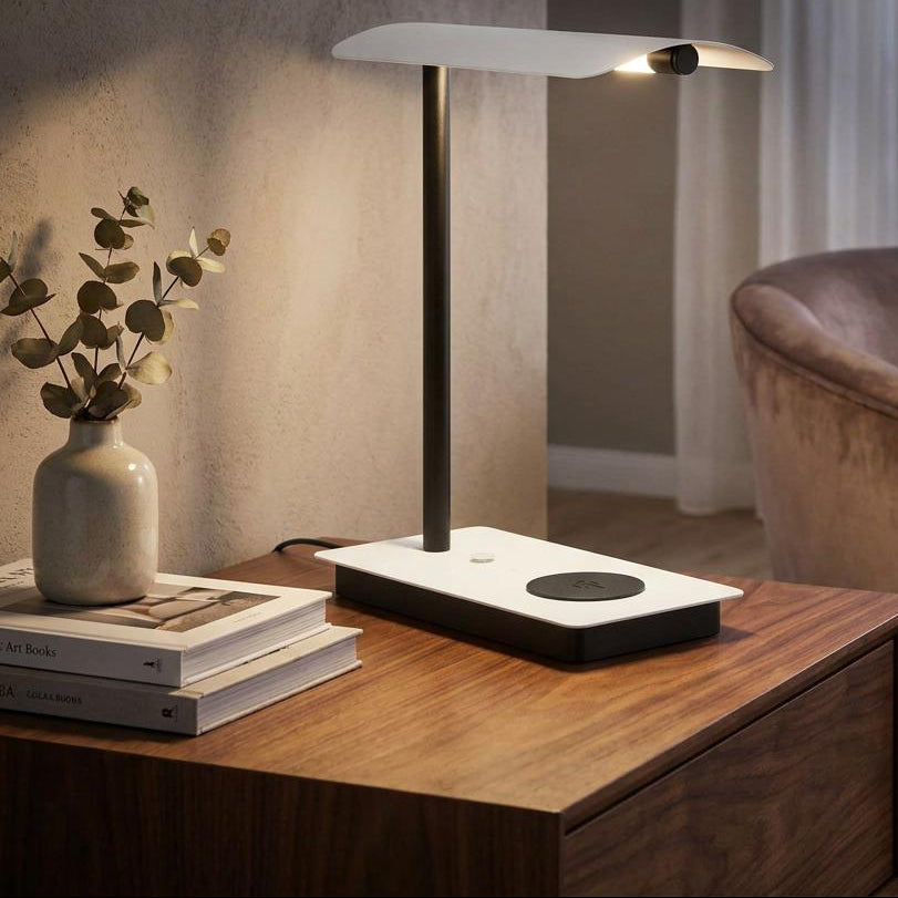 Modern black and white LED table lamp with a curved shade on a wooden desk in a warm living room setting.