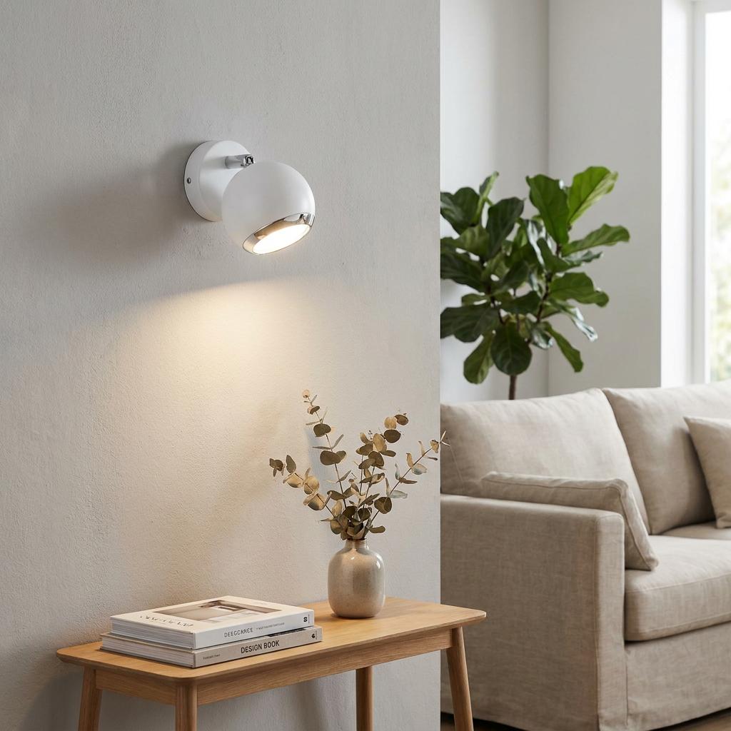 White spherical wall spotlight with chrome accents illuminates a modern living room wall above a wooden side table.