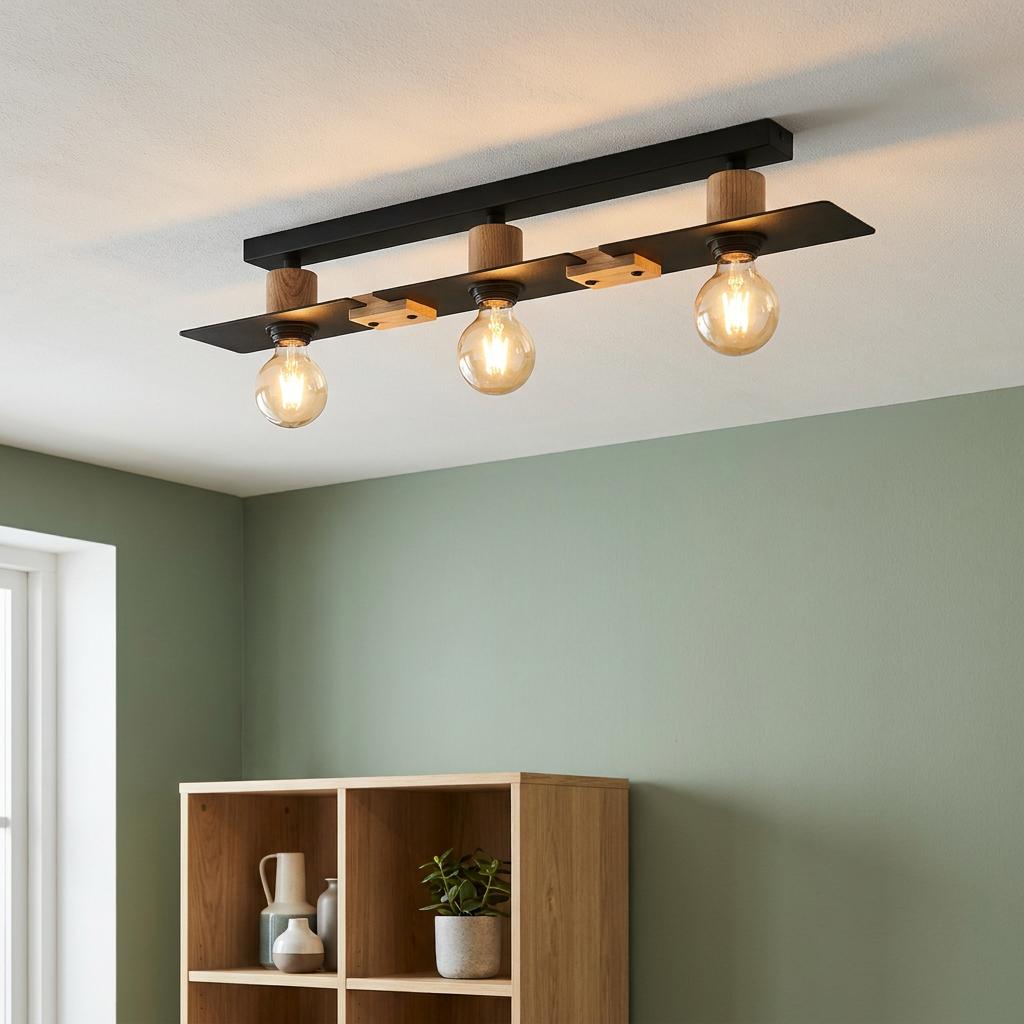 A three-light flush ceiling fixture with black metal and wood accents, illuminating a room with a green wall.