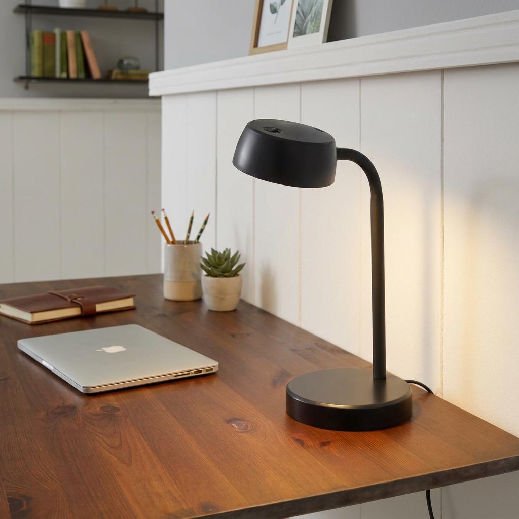 Black matte LED desk lamp illuminating a wooden office desk featuring a laptop and office supplies.