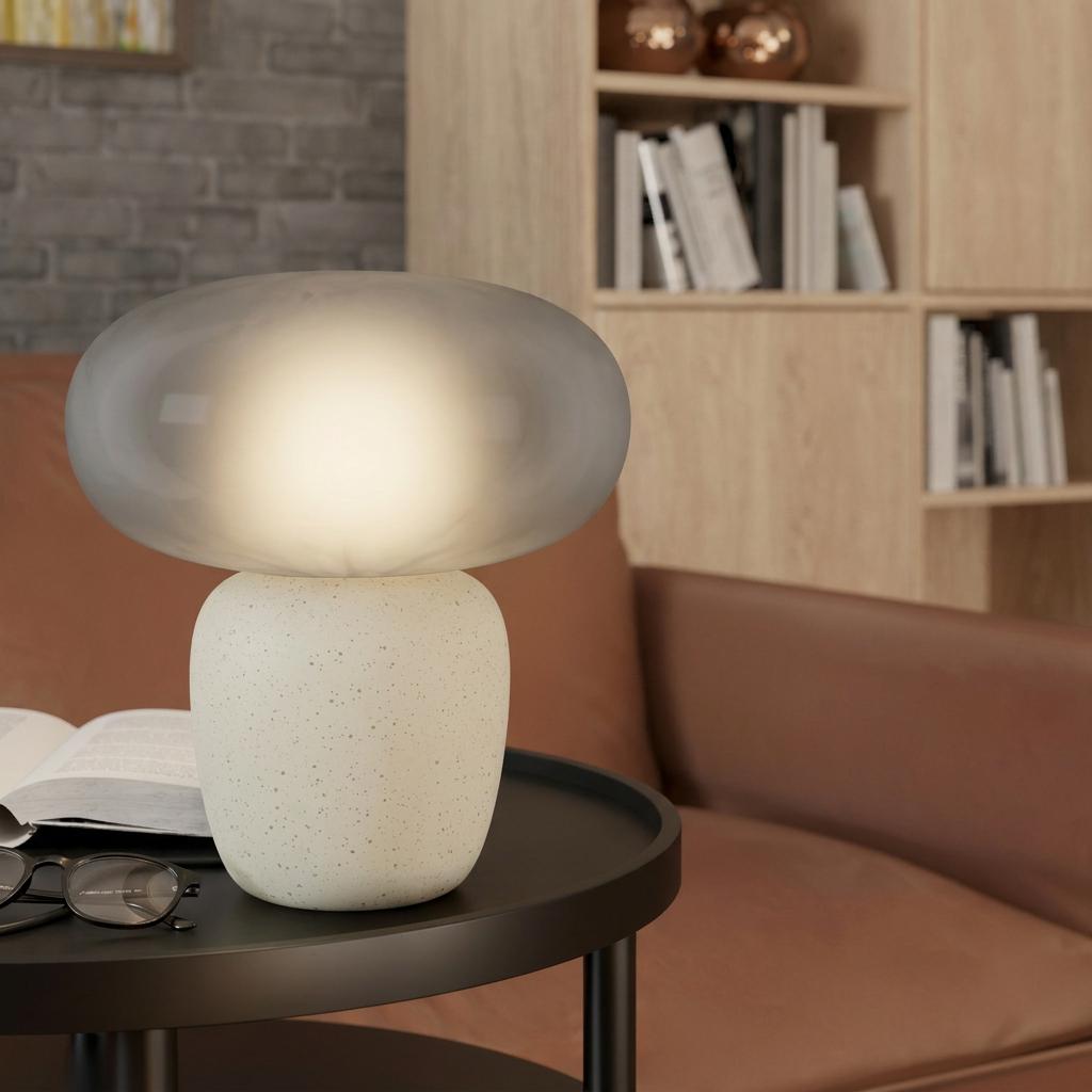 Eglo Cahuama table lamp with a speckled white ceramic base and a glowing satin grey glass shade on a black table.