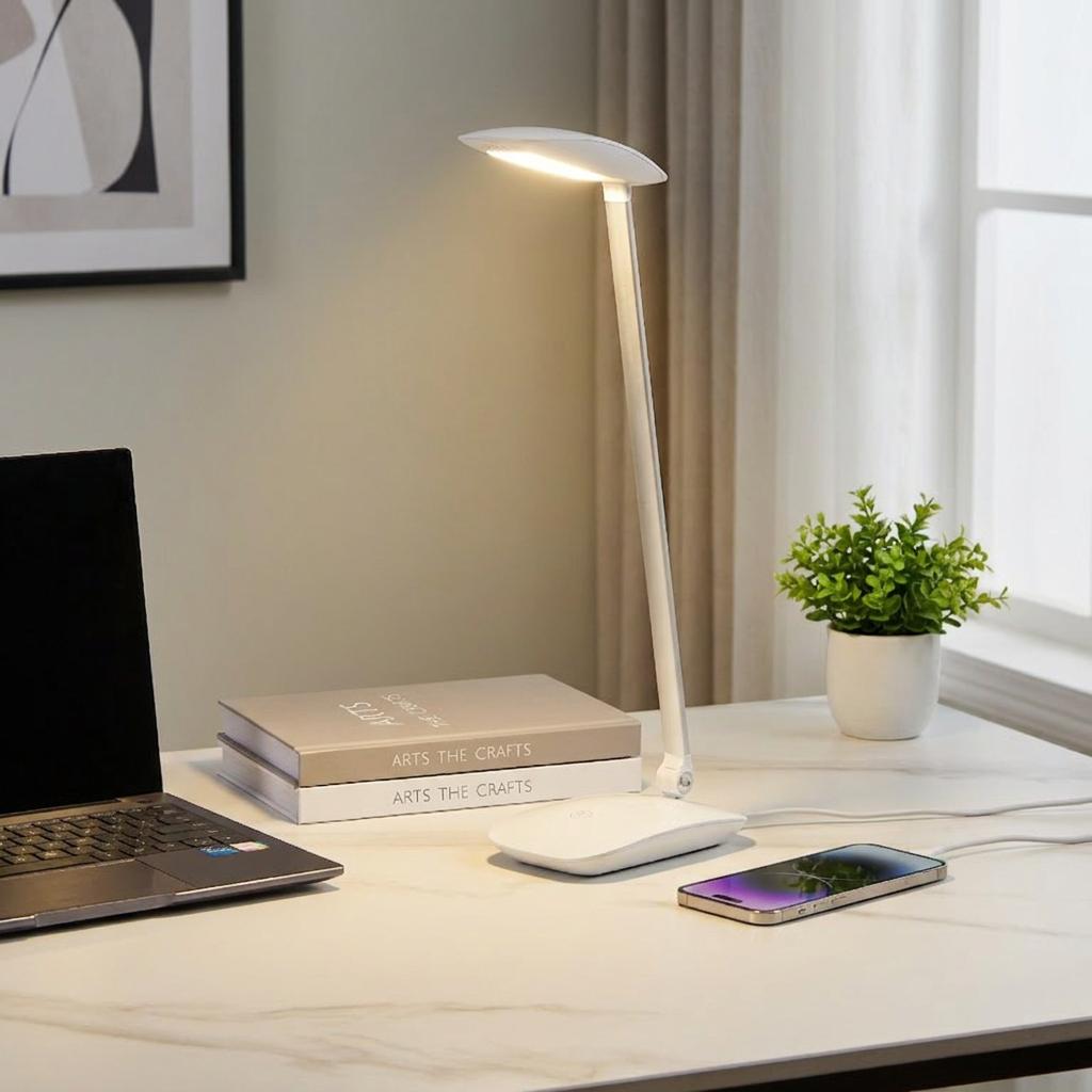 White Eglo Cajero LED desk lamp illuminated on a marble desk next to a laptop and charging smartphone.
