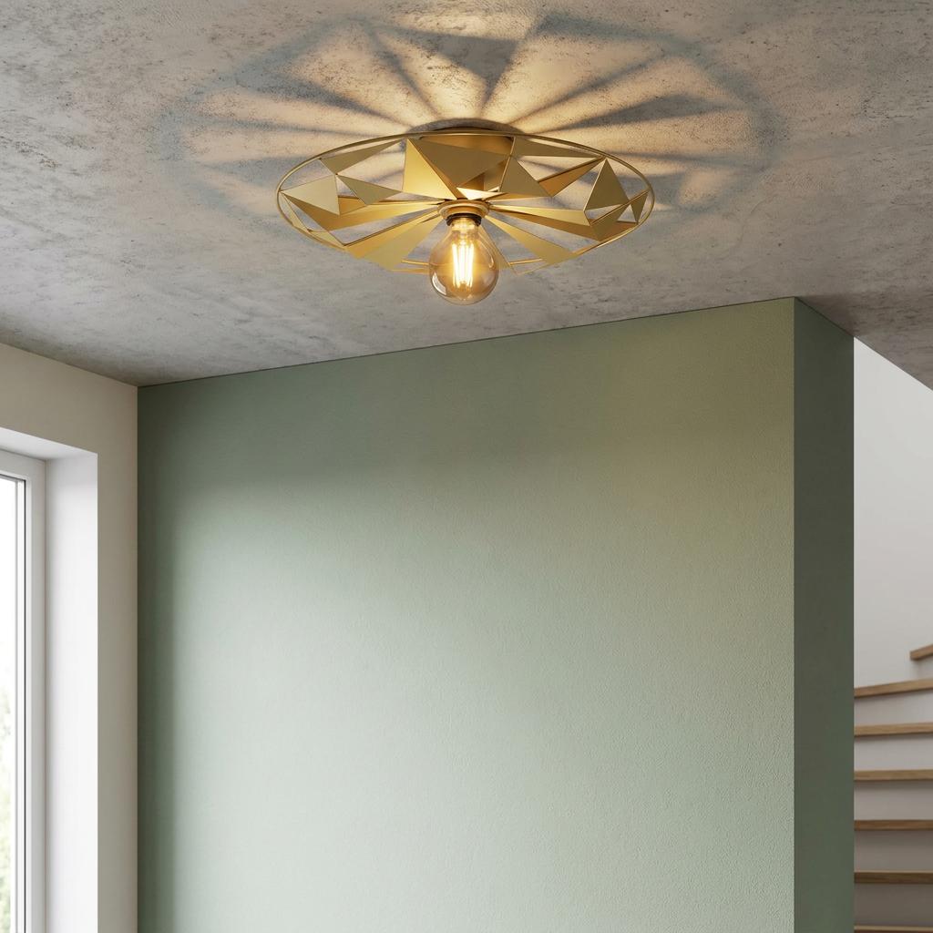 Gold geometric flush ceiling light casting radial shadows on a concrete ceiling above a sage green wall.