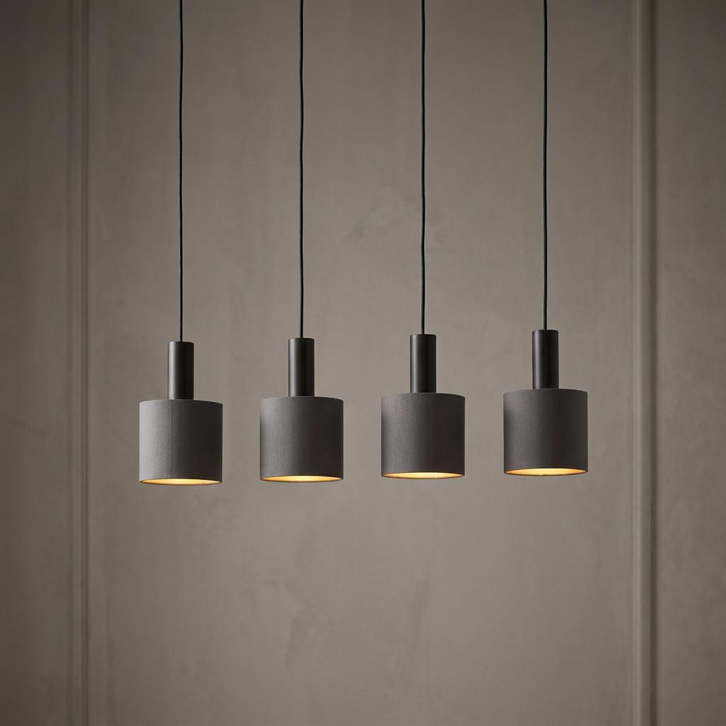 Four dark cylindrical fabric pendant lights with glowing gold interiors hanging against a neutral wall.