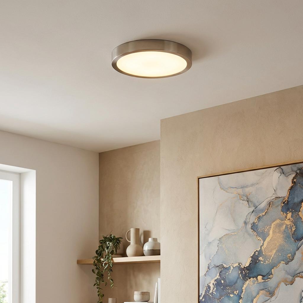 Round nickel flush-mount LED ceiling light emitting warm glow in a modern room with abstract wall art.