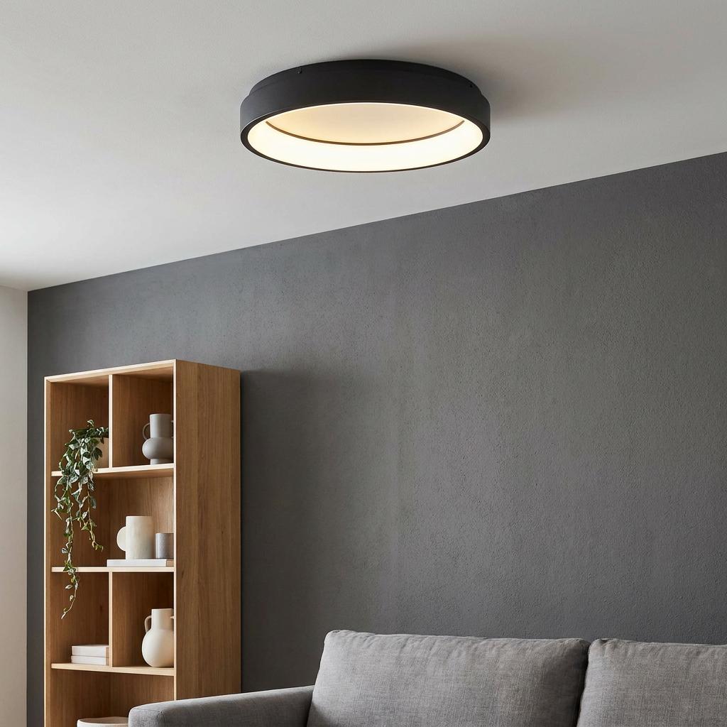 Black ring-shaped LED flush ceiling light in a living room with a grey sofa and dark accent wall.