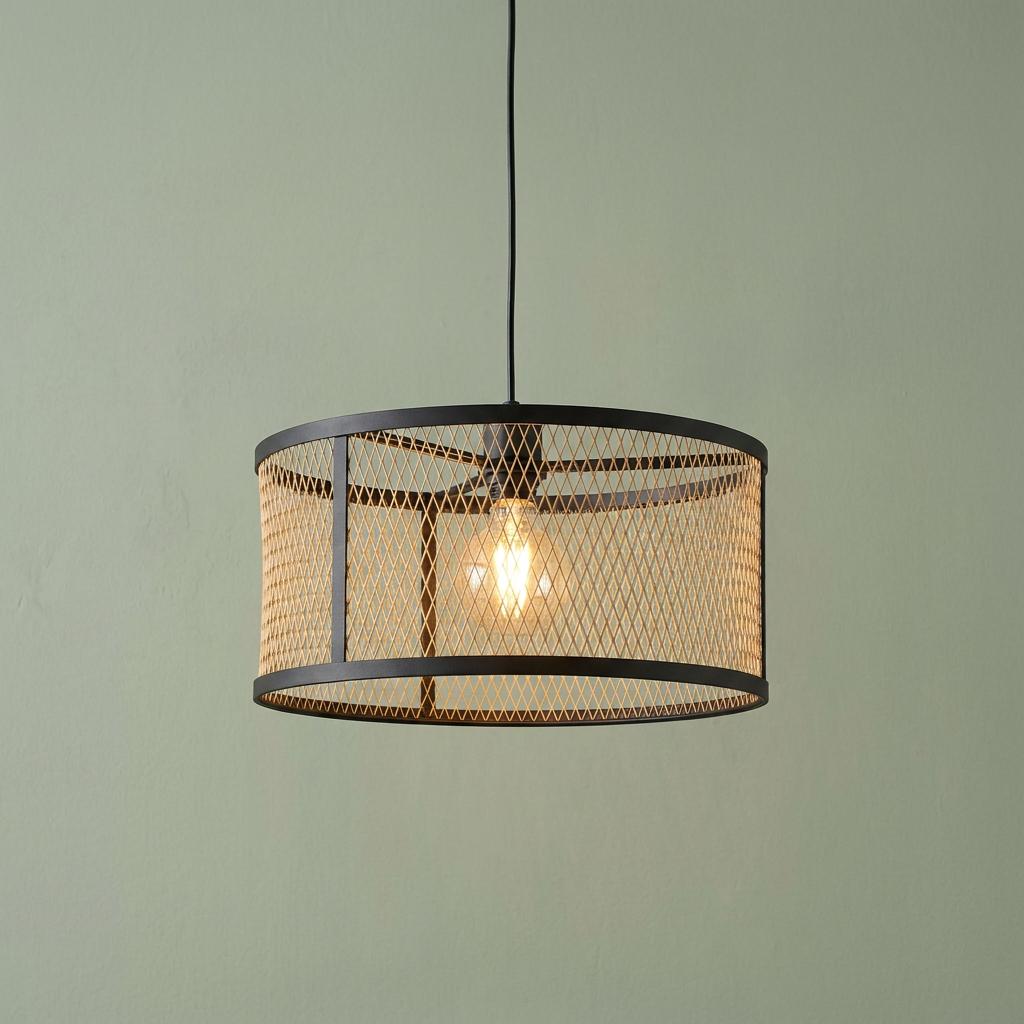 Round black and brass mesh pendant light with an illuminated bulb hanging against a sage green wall.