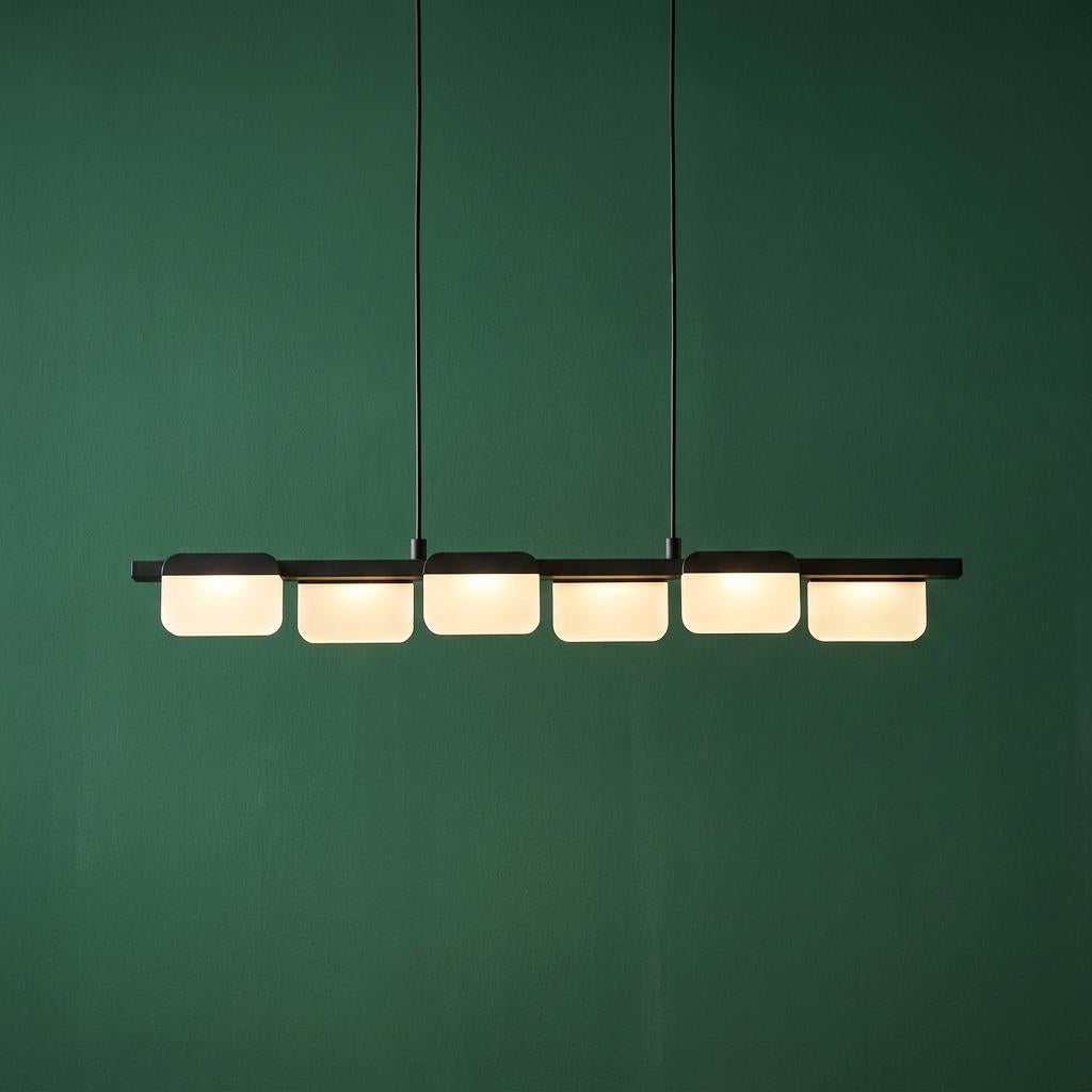 A black linear ceiling pendant with six glowing white square-shaped lights against a dark green wall.