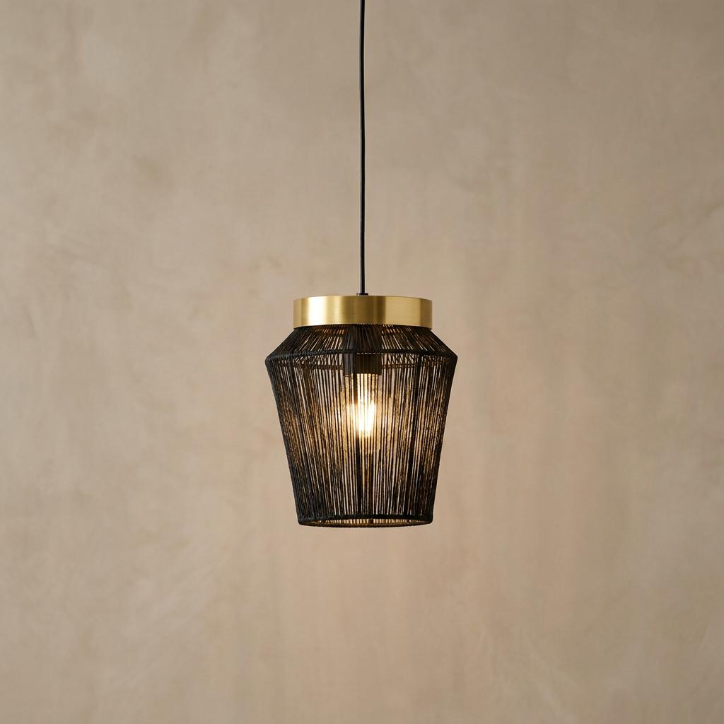 Black wire and gold pendant light with a glowing bulb hanging against a neutral textured wall.