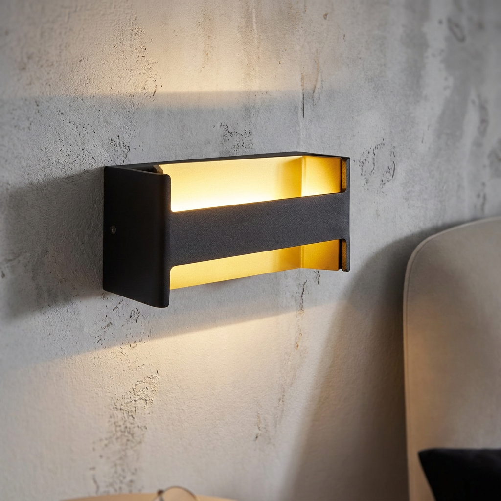 Modern black and gold rectangular LED wall light casting a warm glow on a textured bedroom wall.