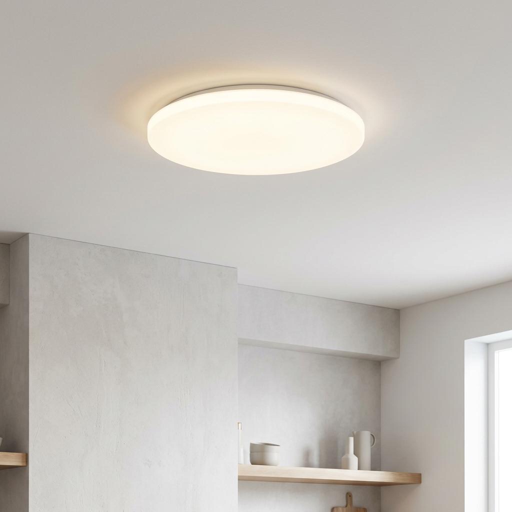 Round white LED flush ceiling light illuminating a minimalist kitchen with a soft, warm glow.