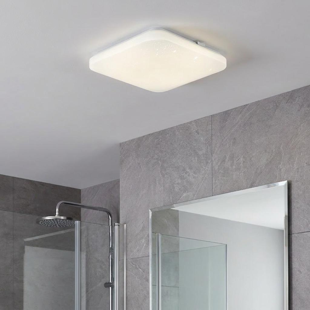 Square white flush LED ceiling light illuminated in a grey tiled bathroom above a shower and mirror.