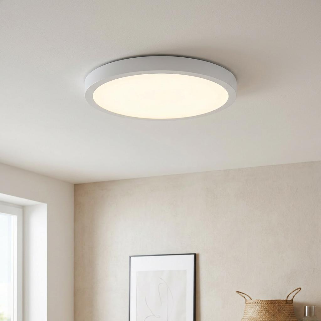 Round white flush-mount LED ceiling light glowing warmly in a modern minimalist room setting.