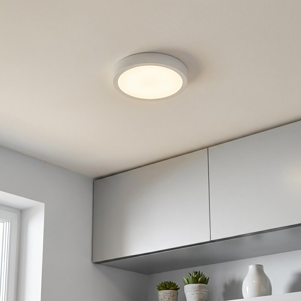 Round white LED flush ceiling light mounted on a plain white ceiling above modern light grey kitchen cabinets.