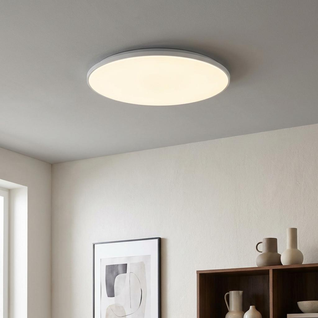 Slim round LED flush ceiling light illuminating a minimalist room with a warm white glow.