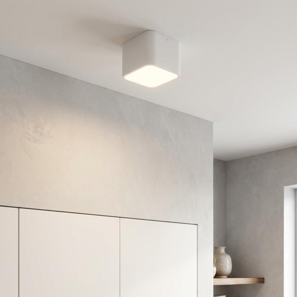 Illuminated white square flush ceiling light mounted in a minimalist room with neutral textured walls.