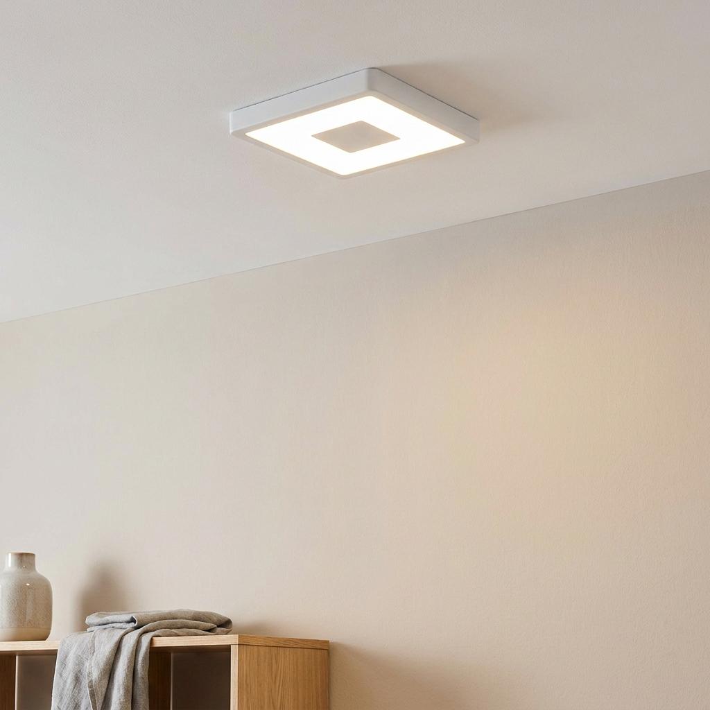 Square white LED flush ceiling light with central opaque detail illuminating a minimalist room.