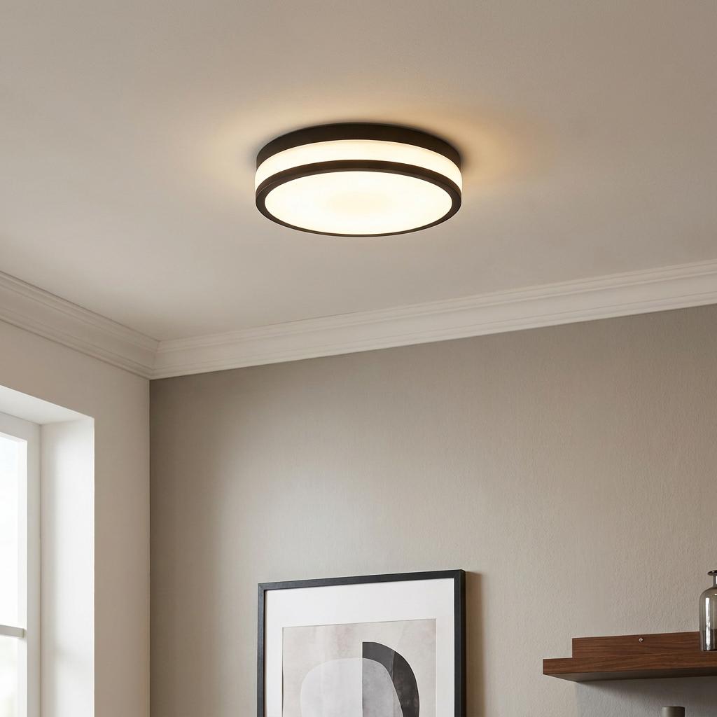 Modern black round flush-mount LED ceiling light with a warm glow, installed in a room with neutral-colored walls.