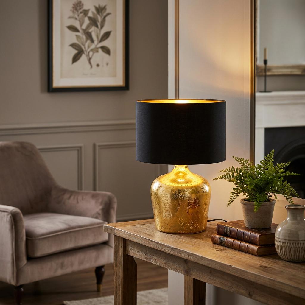A glowing gold table lamp with a black drum shade sits on a rustic wooden table in a well-decorated living room.