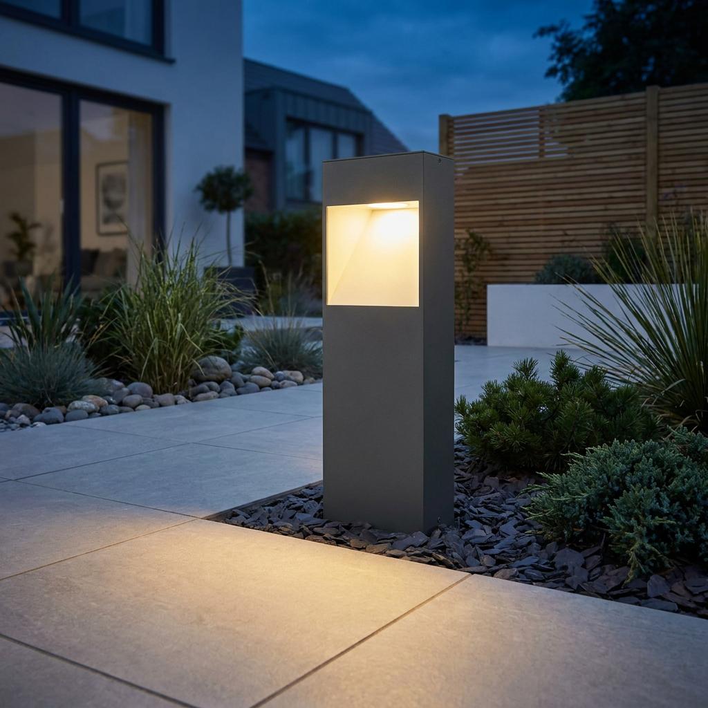 Eglo Manfria grey LED bollard light illuminating a modern tiled patio and garden area at dusk.