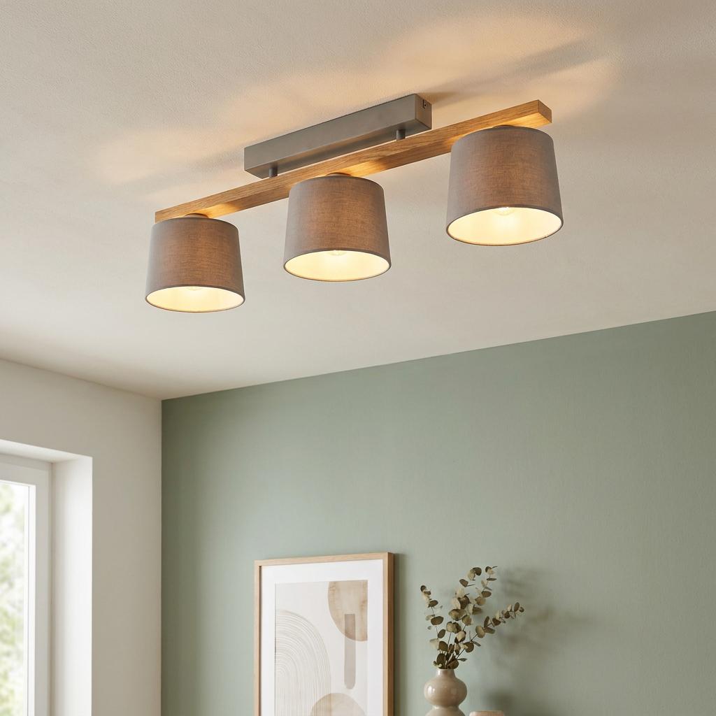 Modern three-light ceiling fixture with grey fabric shades on a natural wood bar, mounted on a white ceiling.