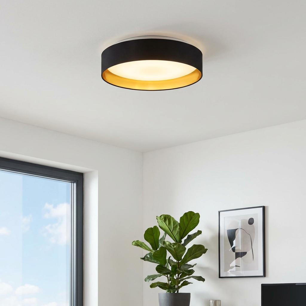 Illuminated round black fabric flush ceiling light with a gold interior in a contemporary white living space.