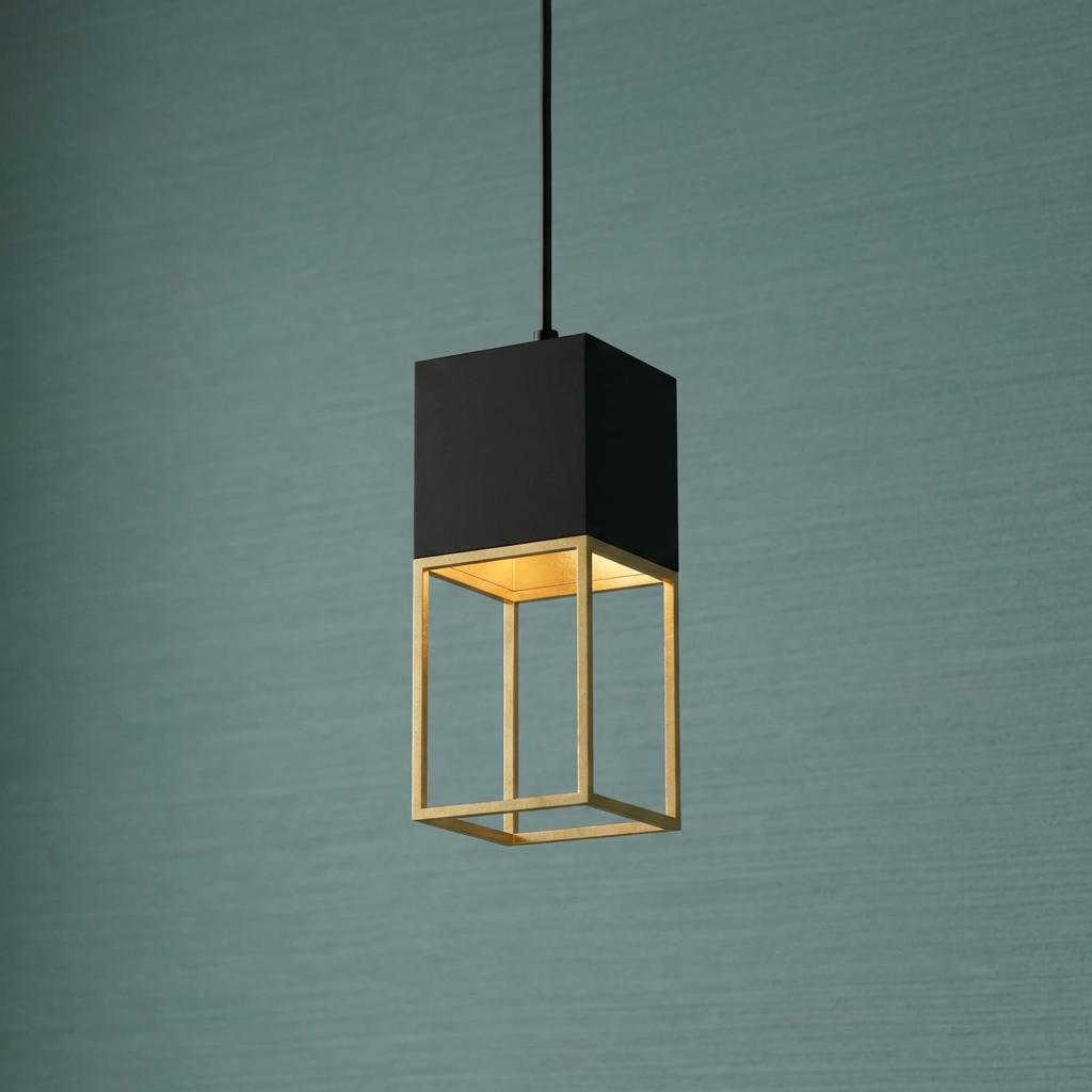 A modern pendant light with a black cube top and a gold open-frame base against a textured teal wall.