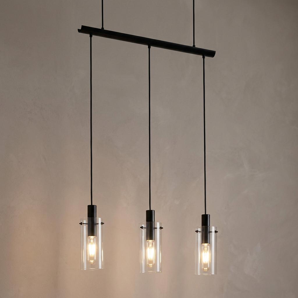 Three clear glass cylinder pendant lights with black hardware hanging from a bar against a neutral textured wall.